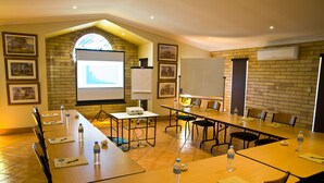 A conference room with long tables, chairs, a projector screen, and framed pictures on the walls. - Starlight Motor Inn (Roma)