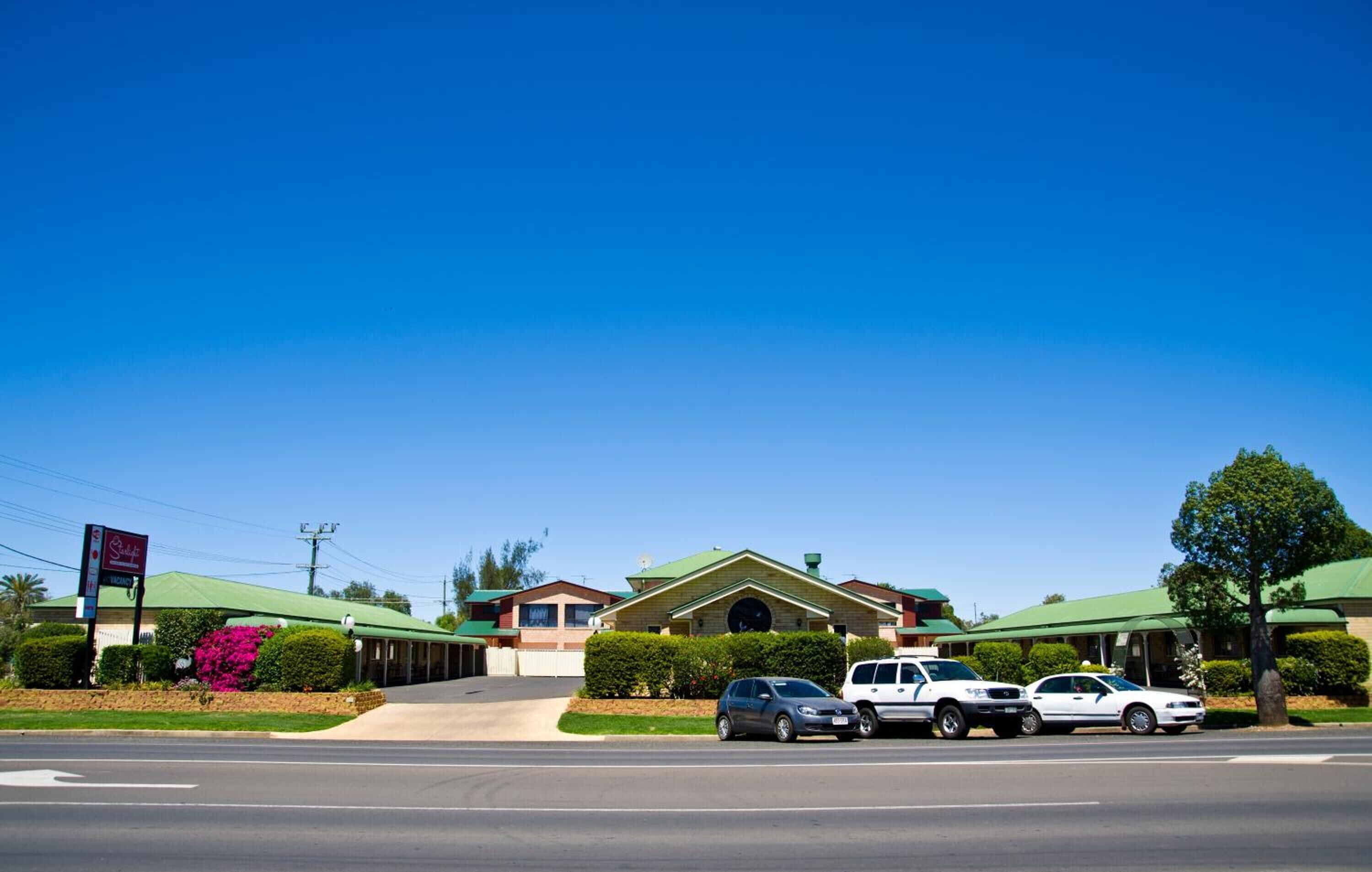 A motel with a green roof, a parking lot, and a signboard.
