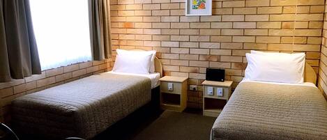 A hotel room with two single beds, a small table, a chair, and a brick wall.