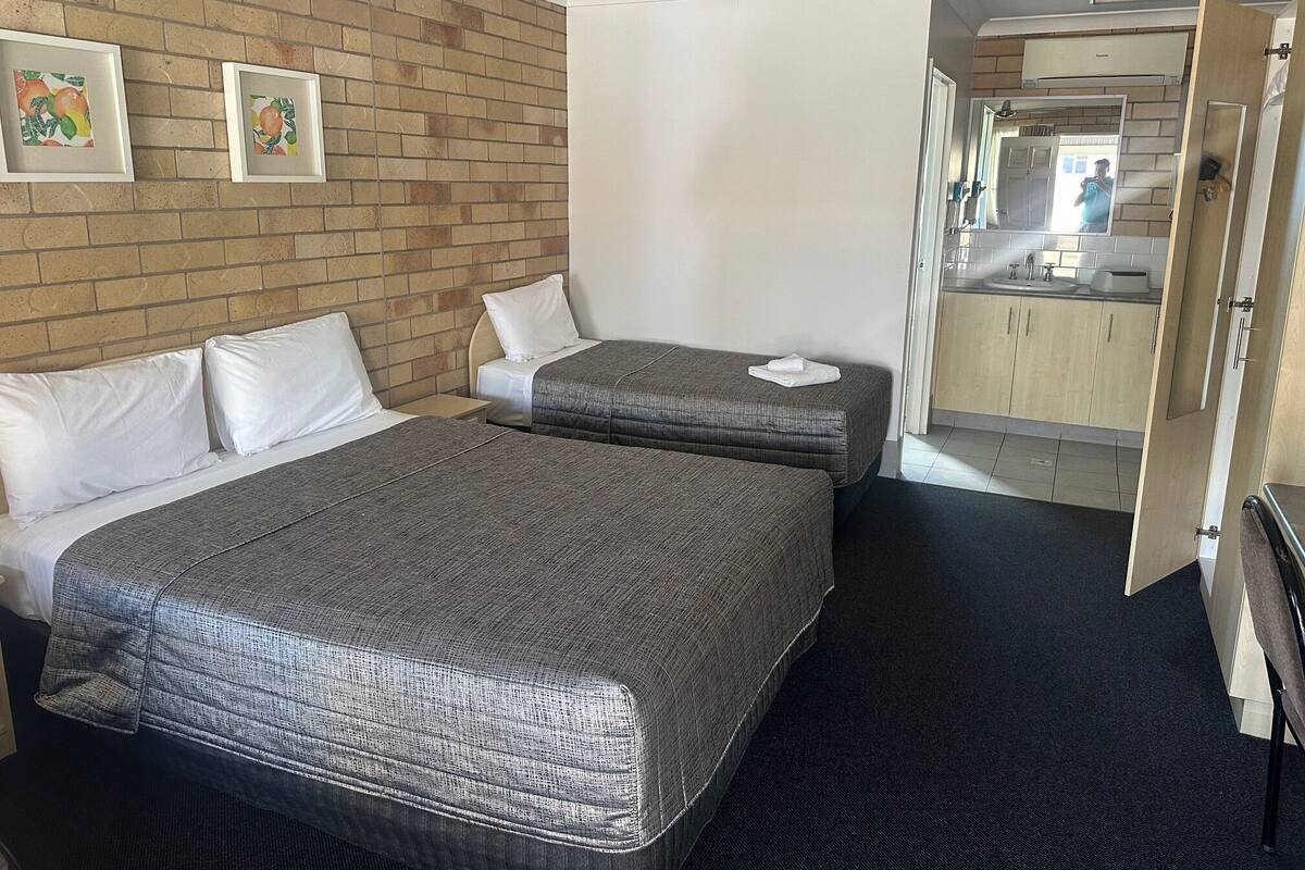 A hotel room with two beds, a brick wall, a kitchenette, and a bathroom visible through an open door.