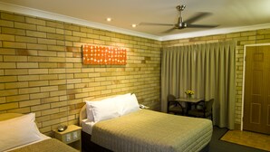 A hotel room with a brick wall, a bed, a desk with a chair, and a door. - Starlight Motor Inn (Roma)