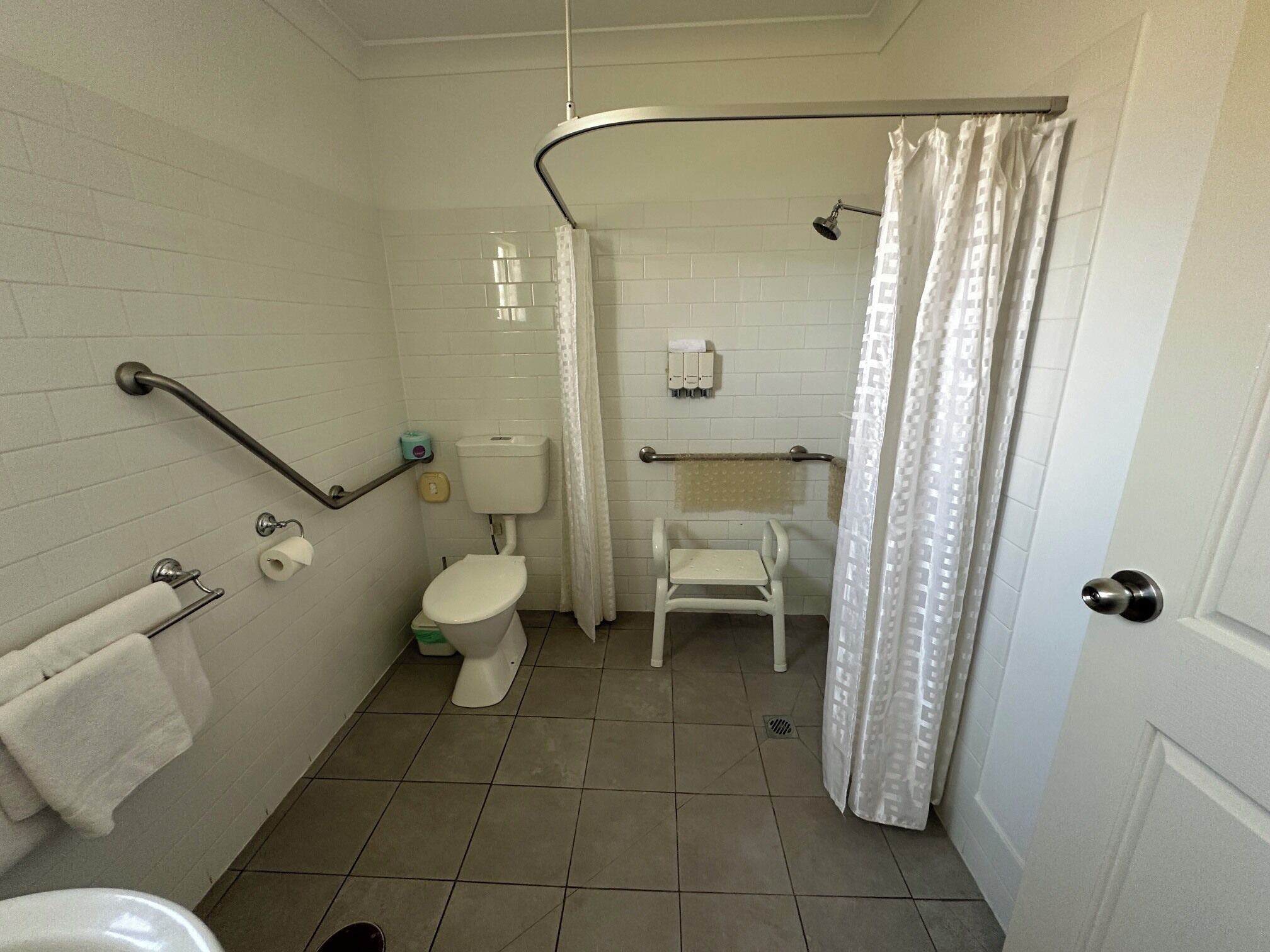 A bathroom with a toilet, a handrail, a shower curtain, and a towel rack.