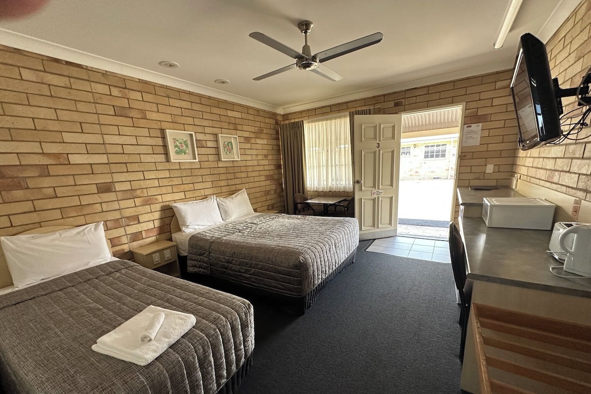 A hotel room with two beds, a desk, a television, and a door leading outside.