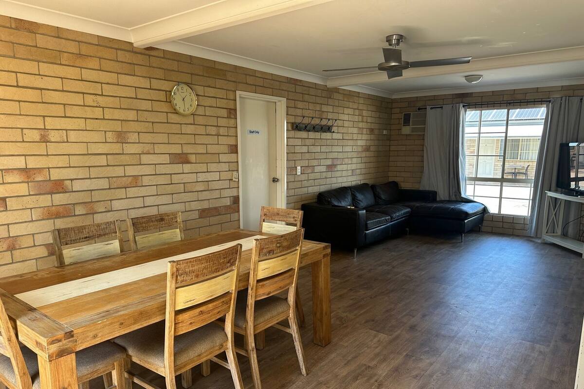 A spacious room with a wooden dining table, chairs, a black leather sofa, and a brick wall.