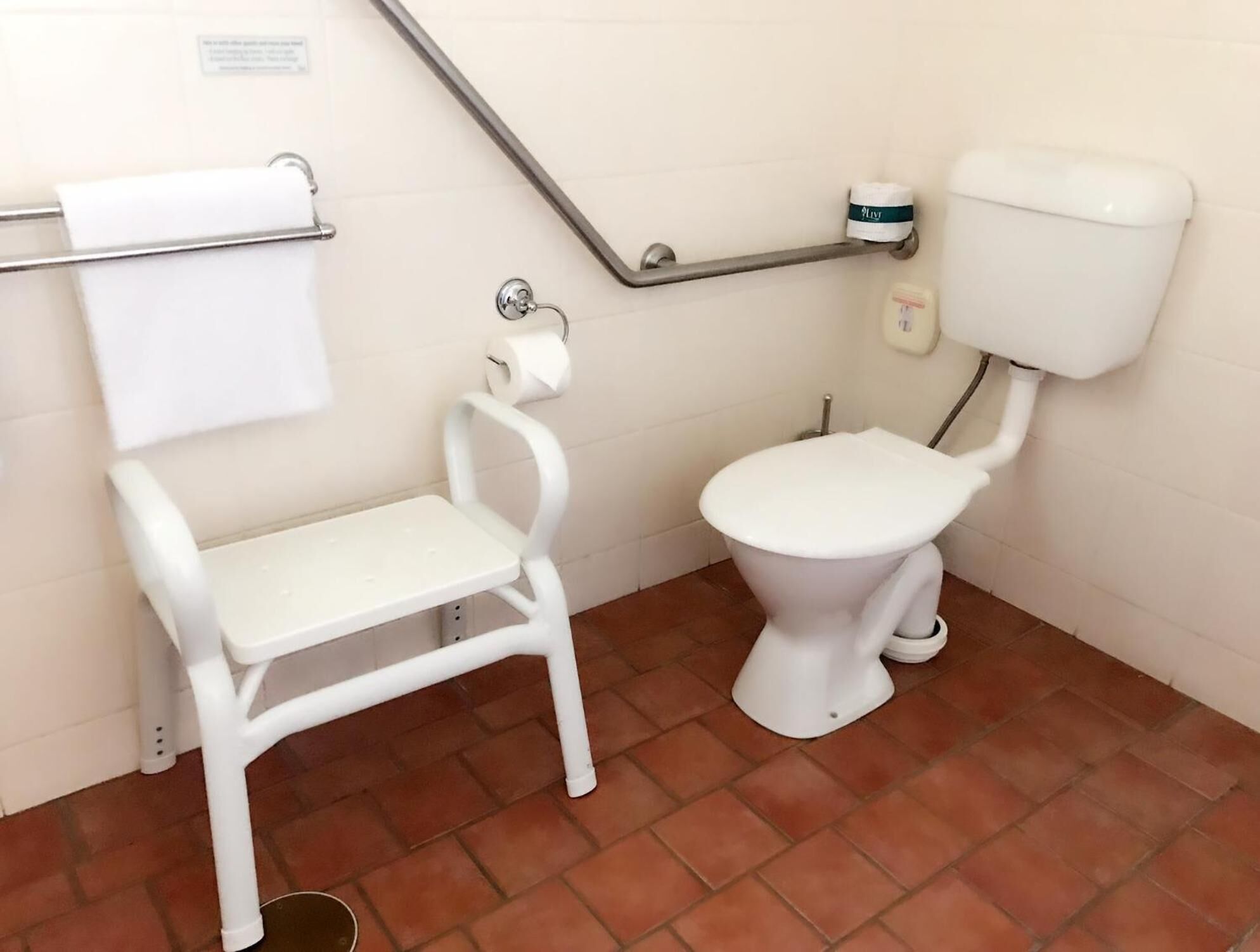 Et lille, rent badeværelse med toilet i hvidt, et hvidt siddebænk og gelænder.