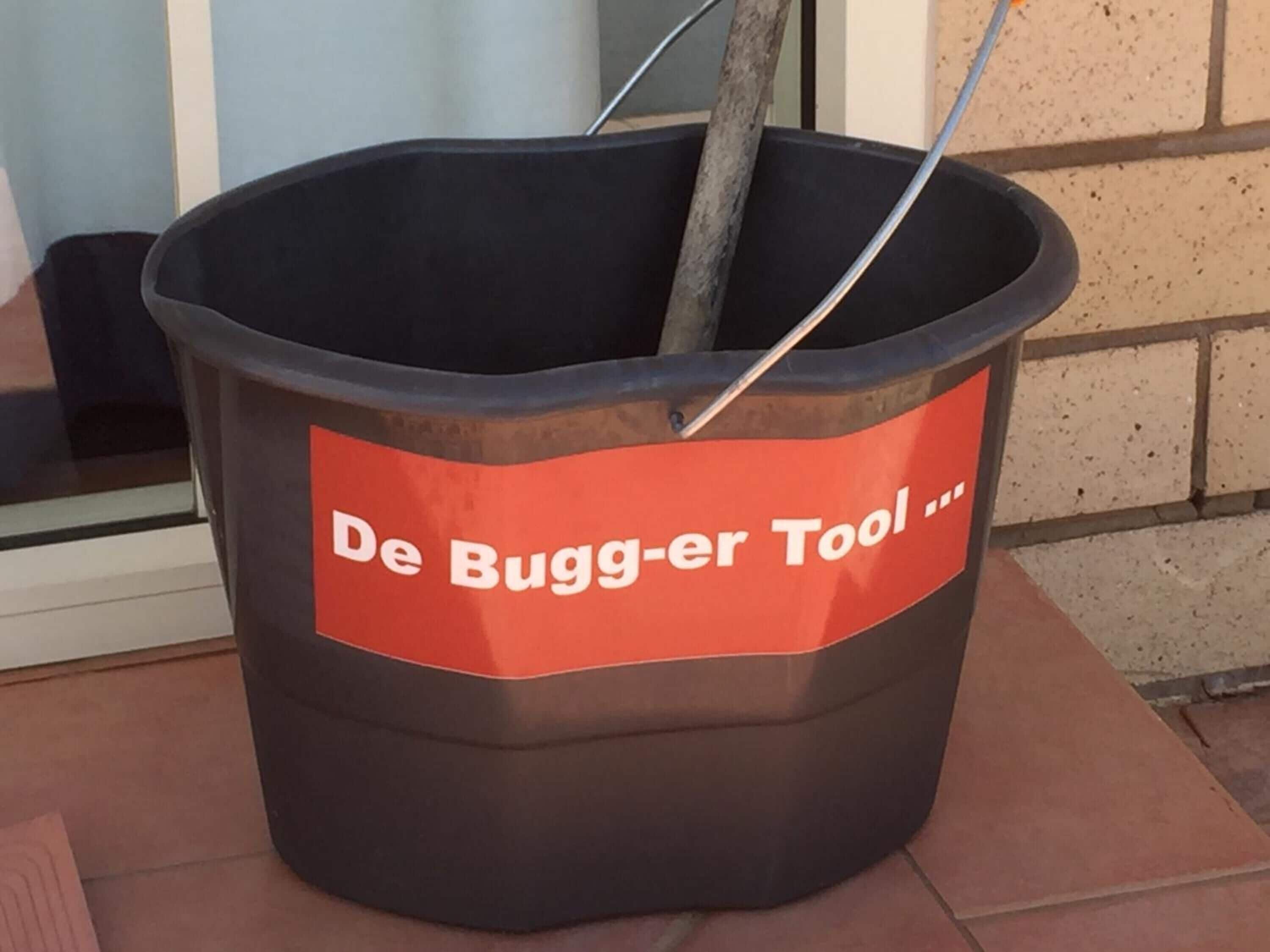 A trash bin labeled "De Bugger-er Tool" with a metal pole inside.