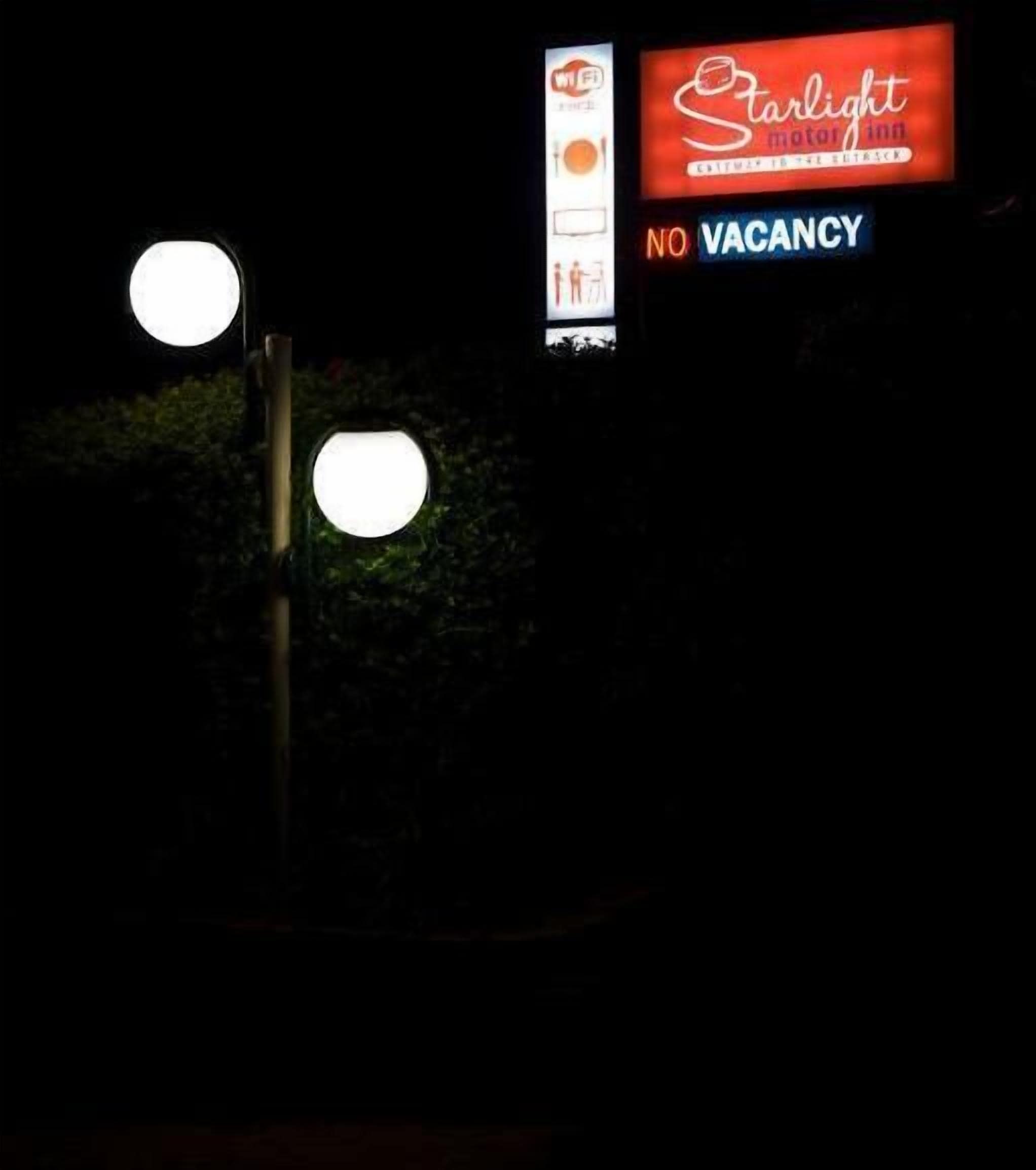 A nighttime view of a street with a 'Starlight Motor Inn' sign indicating no vacancy.