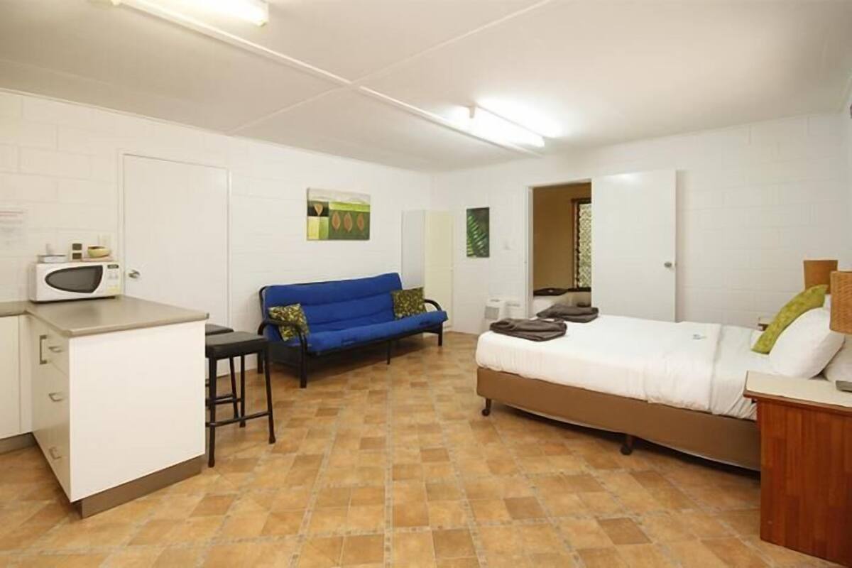 A compact room with a kitchenette, a bed, a blue sofa, and a small table.