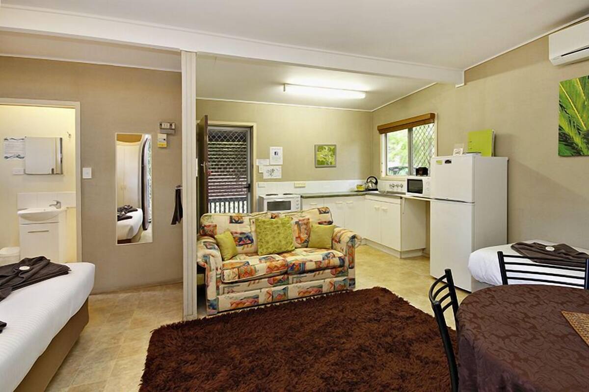 A compact hotel room with a kitchenette, a sofa, a bed, and a bathroom.