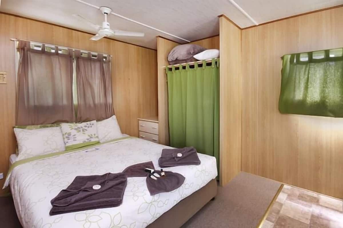 A hotel room with a bed, a green curtain, a ceiling fan, and a green towel on the bed.