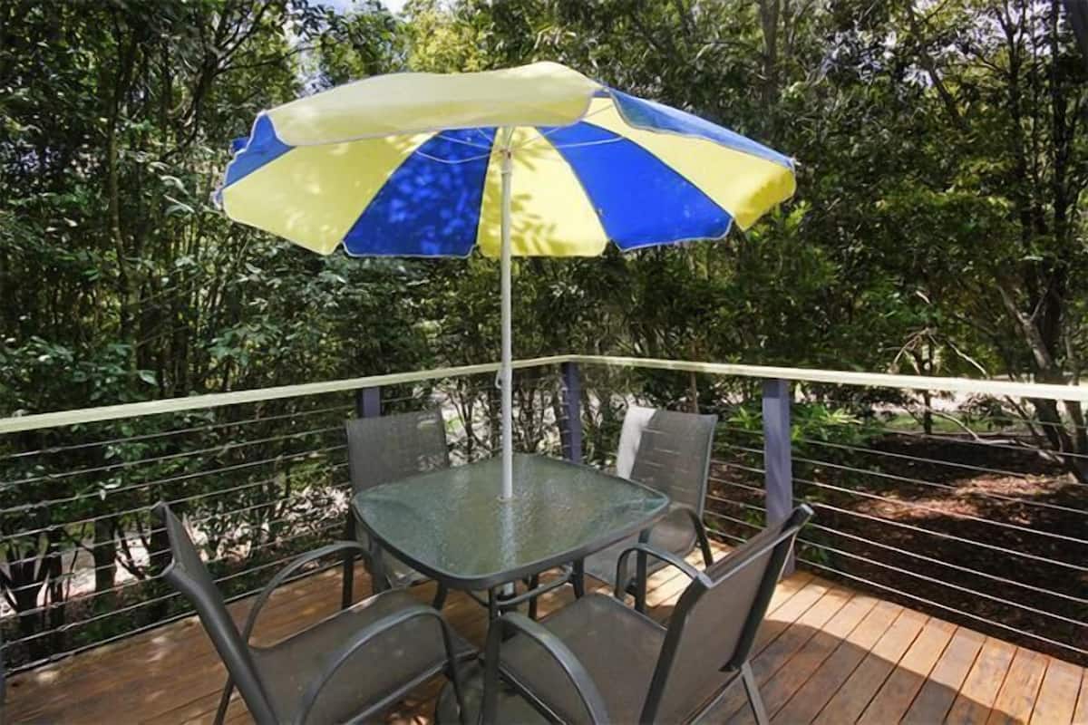 A glass table with four chairs and a blue and yellow striped umbrella.