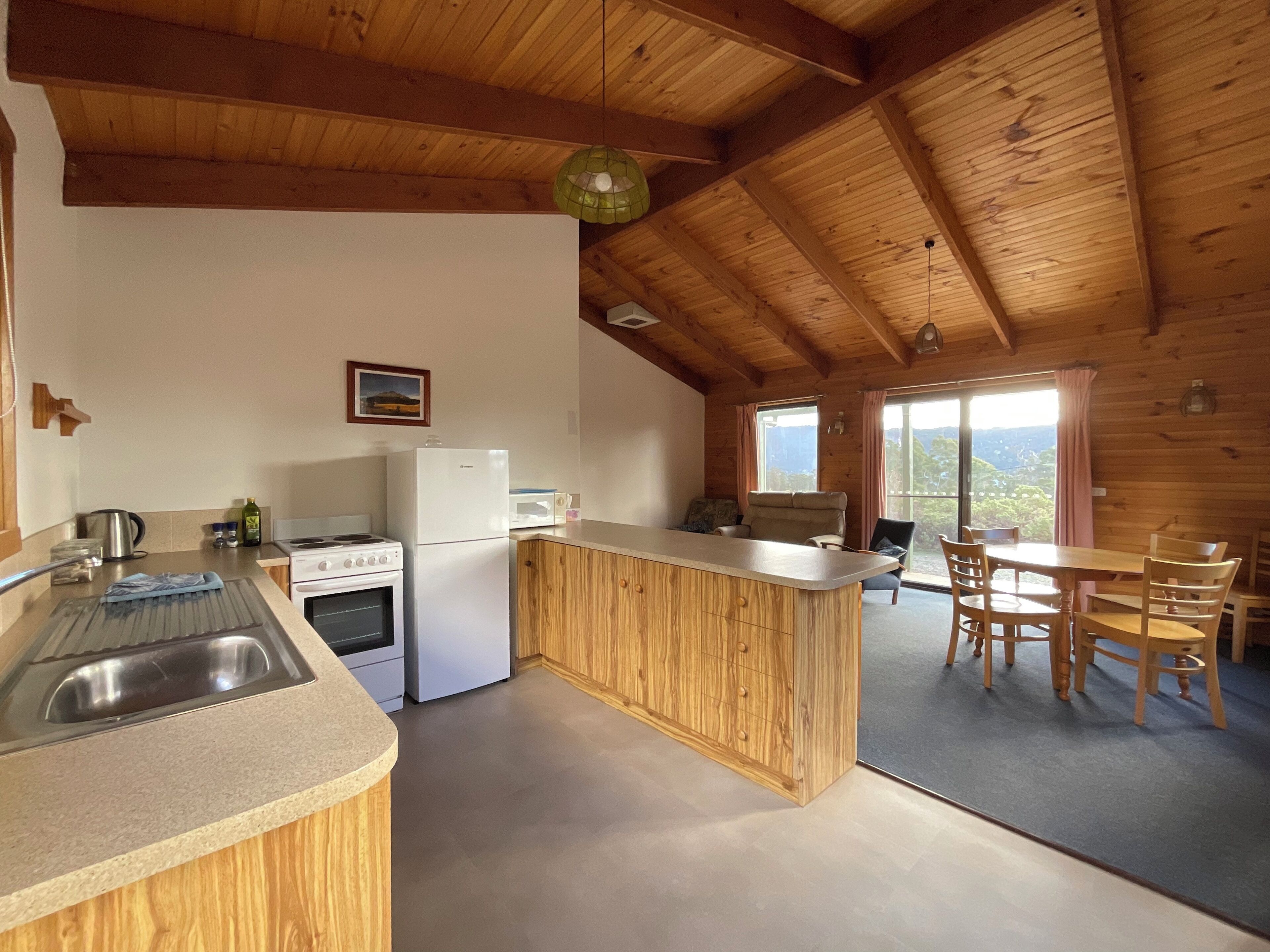 A kitchen with wooden cabinets, a stove, a refrigerator, and a sink. There is a dining area with a table and chairs.