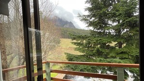 A view from a balcony with a wooden railing, overlooking a pond and a forested area with mountains in the background. - Silver Ridge Retreat (Claude Road)