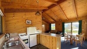 A wooden cabin with a kitchen area featuring a sink, stove, refrigerator, and a dining table with chairs. - Silver Ridge Retreat (Claude Road)