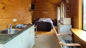 A compact cabin-style room with a wooden interior, a bed, a small kitchenette, and a window providing natural light. - Silver Ridge Retreat (Claude Road)