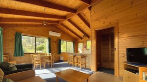 A wooden cabin interior with a sofa, dining table, chairs, a kitchen area, and a TV. - Silver Ridge Retreat (Claude Road)