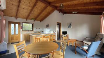 A spacious living area with a wooden ceiling, a dining table with chairs, a sofa, and a television.