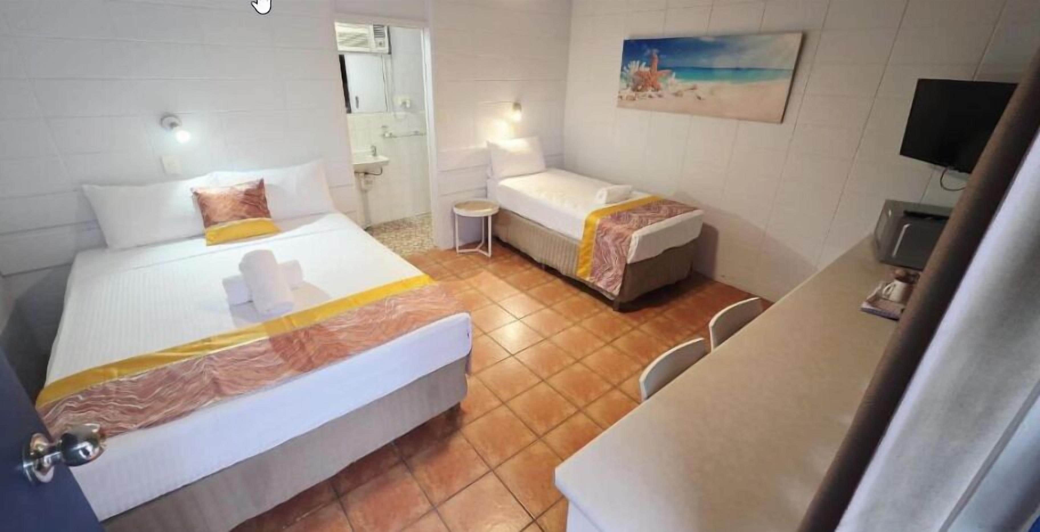 A hotel room with two beds, a small bathroom, a TV, and a painting on the wall.