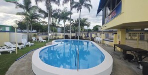 A swimming pool with lounge chairs, palm trees, and a building with a sign. - Sunburst Motel (Biggera Waters)
