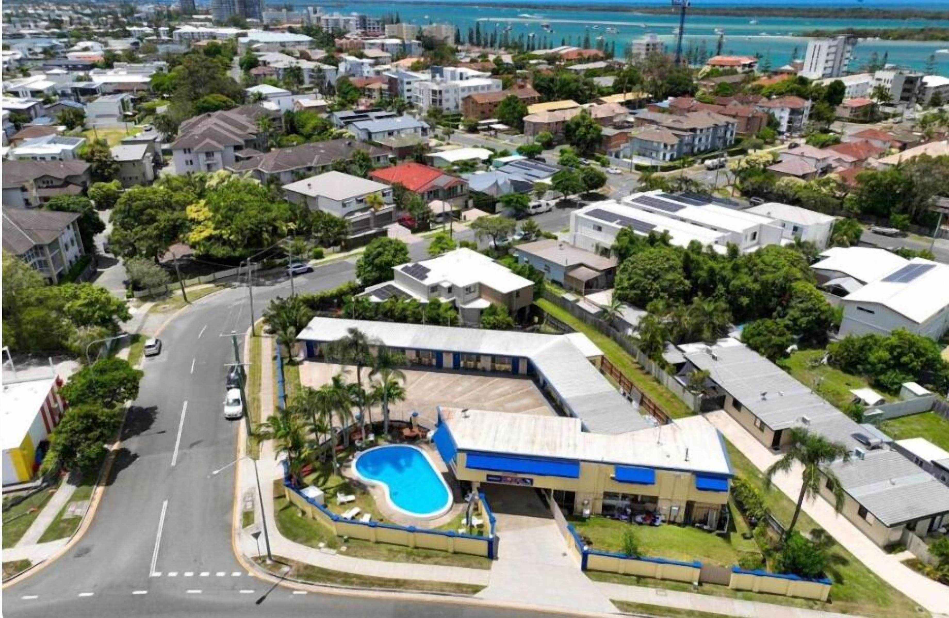 Un barrio residencial con piscina, una calle y un edificio de techo azul.