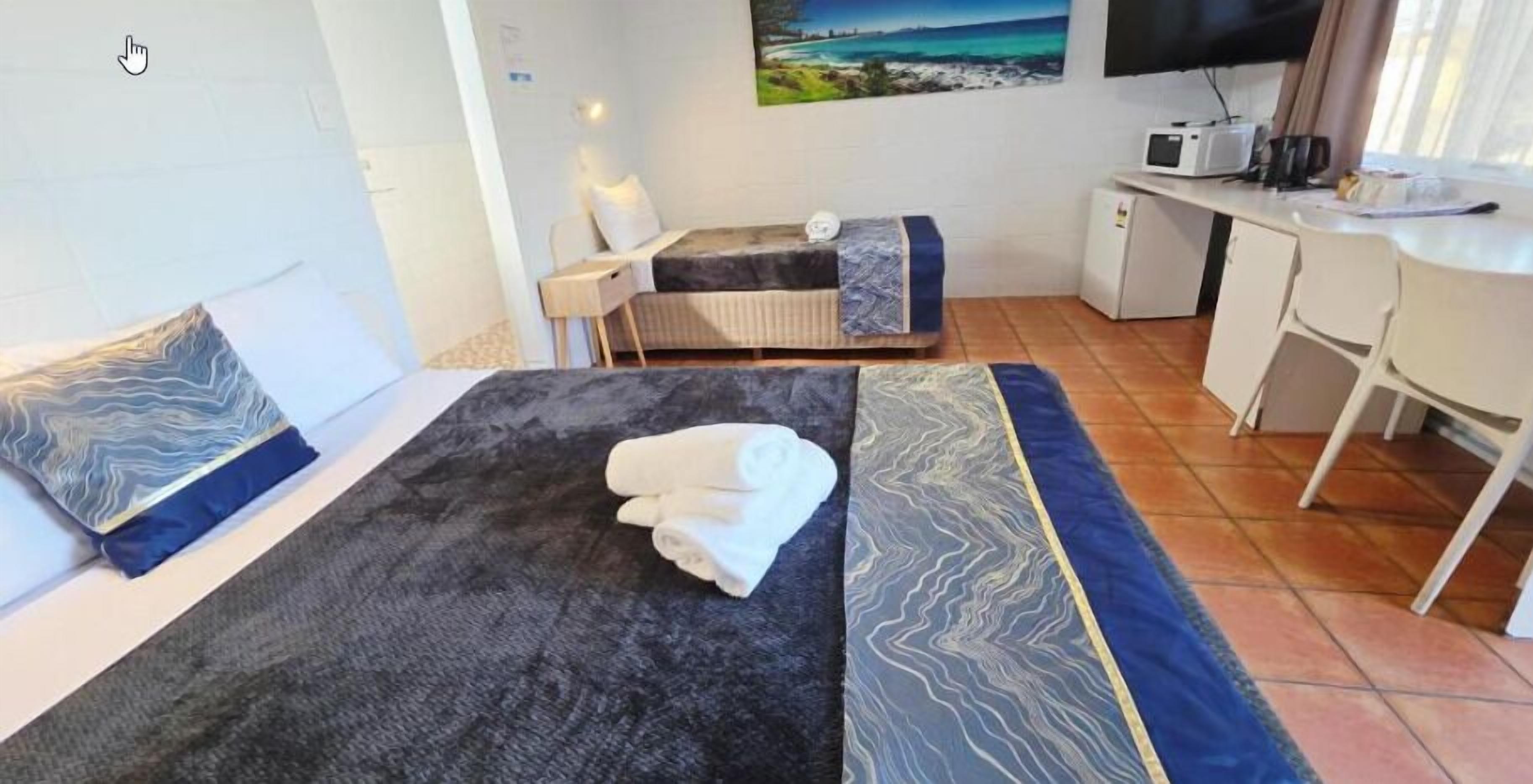A hotel room with a bed, a desk, a chair, a television, and a painting on the wall.