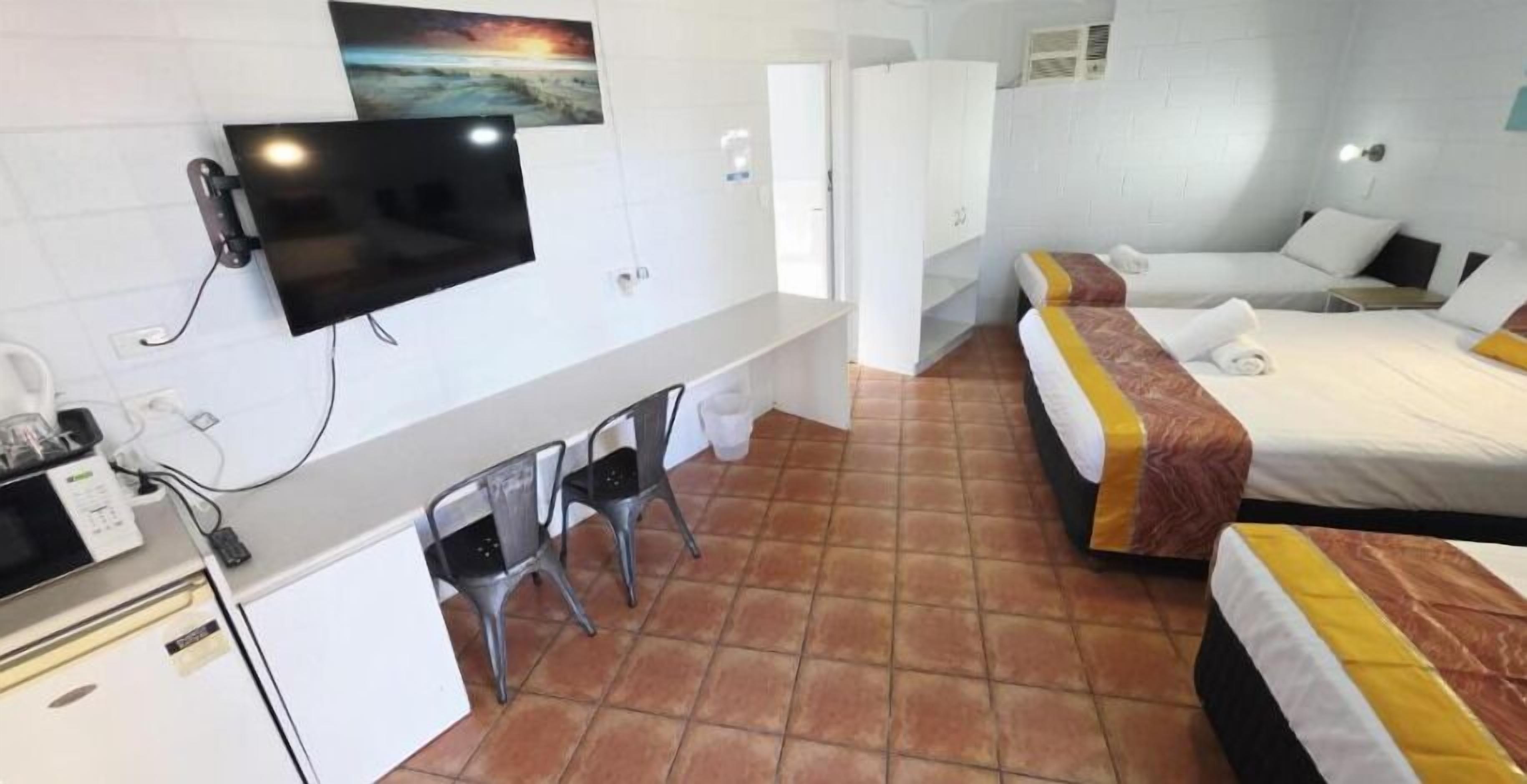 A hotel room with a TV, a desk, two beds, and a bathroom.
