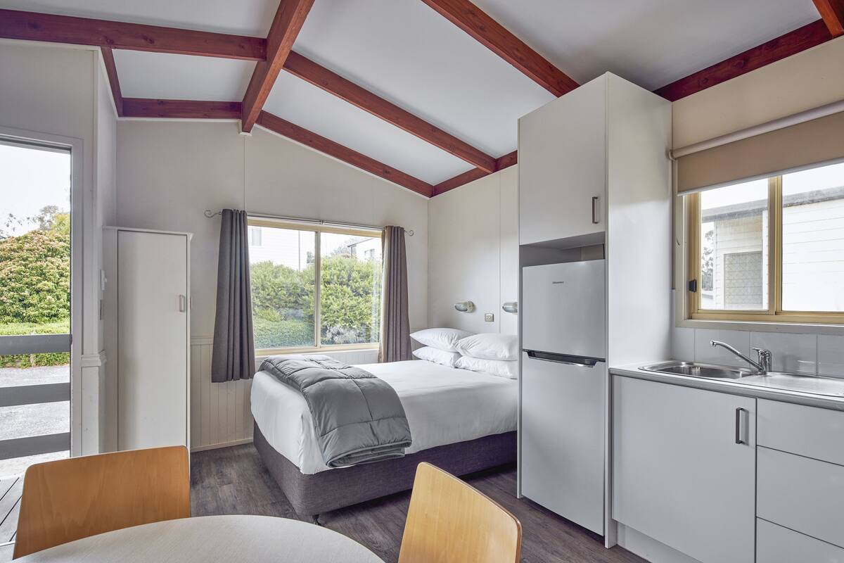 Un dormitorio con cama, una kitchenette pequeña y un ventanal con cortinas.