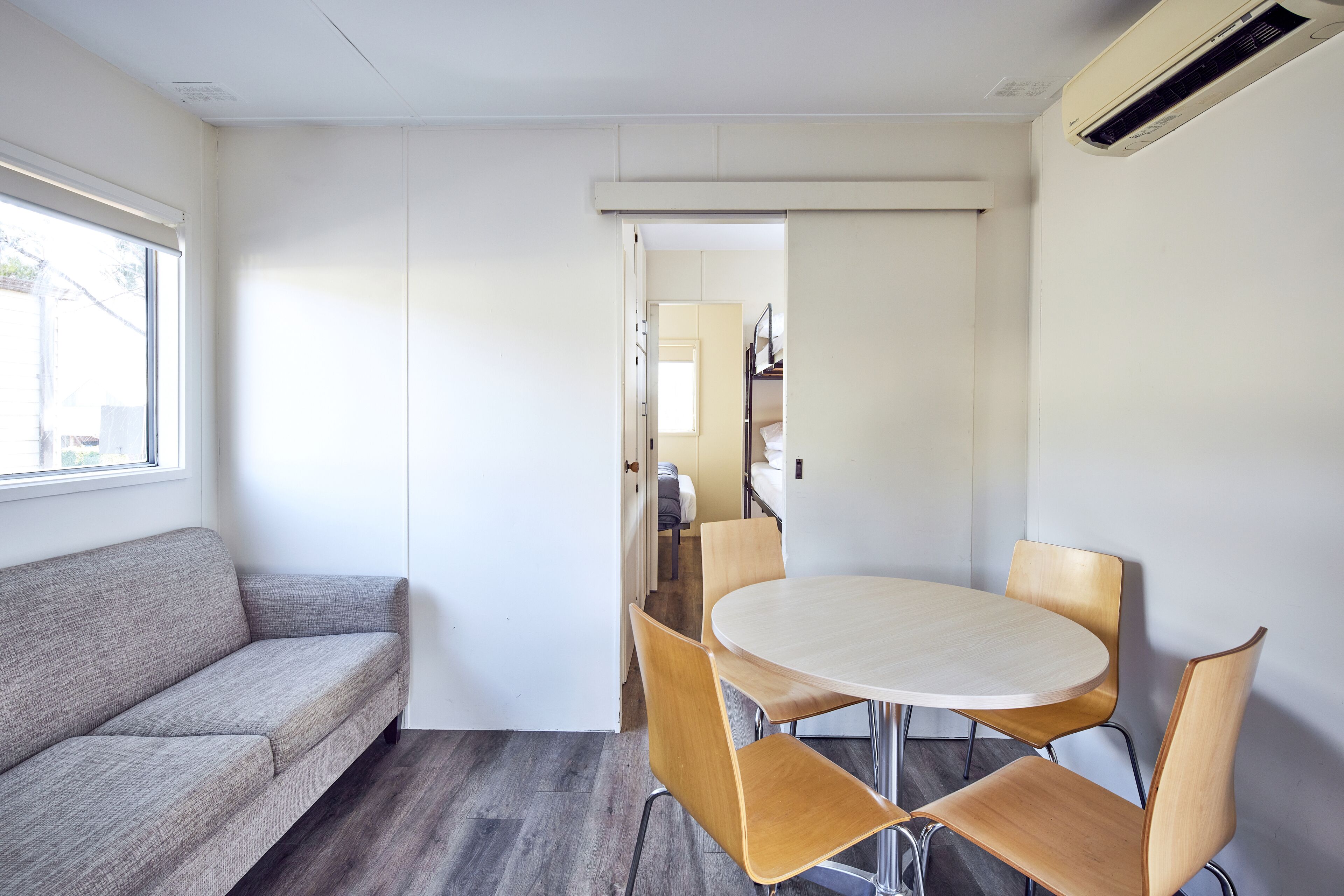 A modern room with a sofa, a round table with four chairs, and a sliding door leading to a kitchen area.