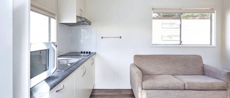 A compact kitchen with white cabinets, a microwave, and a window with blinds.