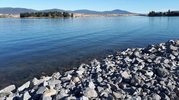 Eine felsige Küstenlinie mit klarem Wasser und Bergen in der Ferne.