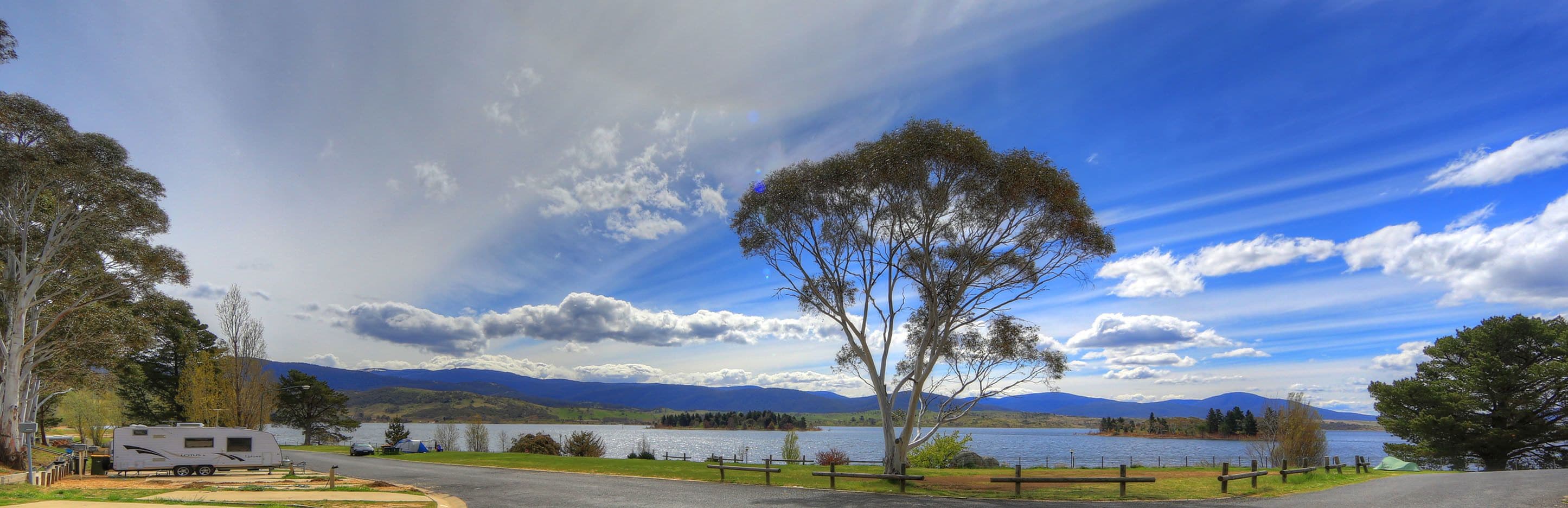 A lakeside camping area with RVs, a picnic table, and a view of mountains.