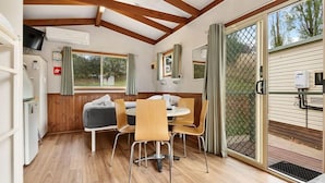 Ein gemütliches Interieur mit Holzbalkendecke, einem Esstisch mit Stühlen, einer kleinen Couch und einem Fenster mit Vorhängen.