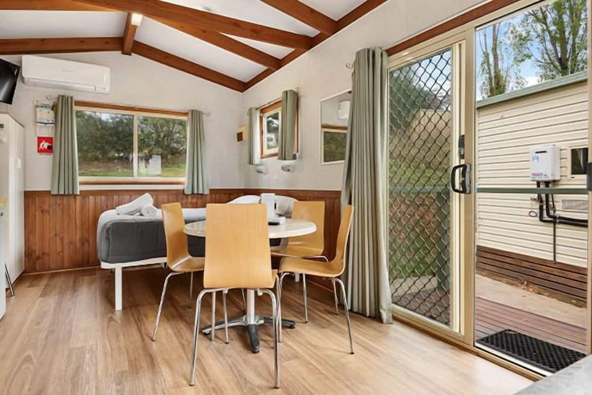 Un interior acogedor con techo de madera, una mesa de comedor con sillas, un pequeño sofá y una ventana con cortinas.