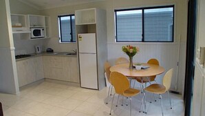 Cocina compacta con armarios blancos, microondas y refrigerador. Hay una mesa de comedor con cuatro sillas y un florero con flores.