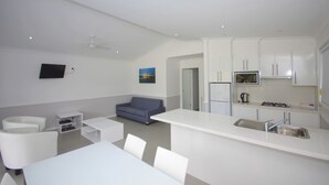 Una cocina moderna con armarios blancos, un comedor con mobiliario blanco y un sofá gris.