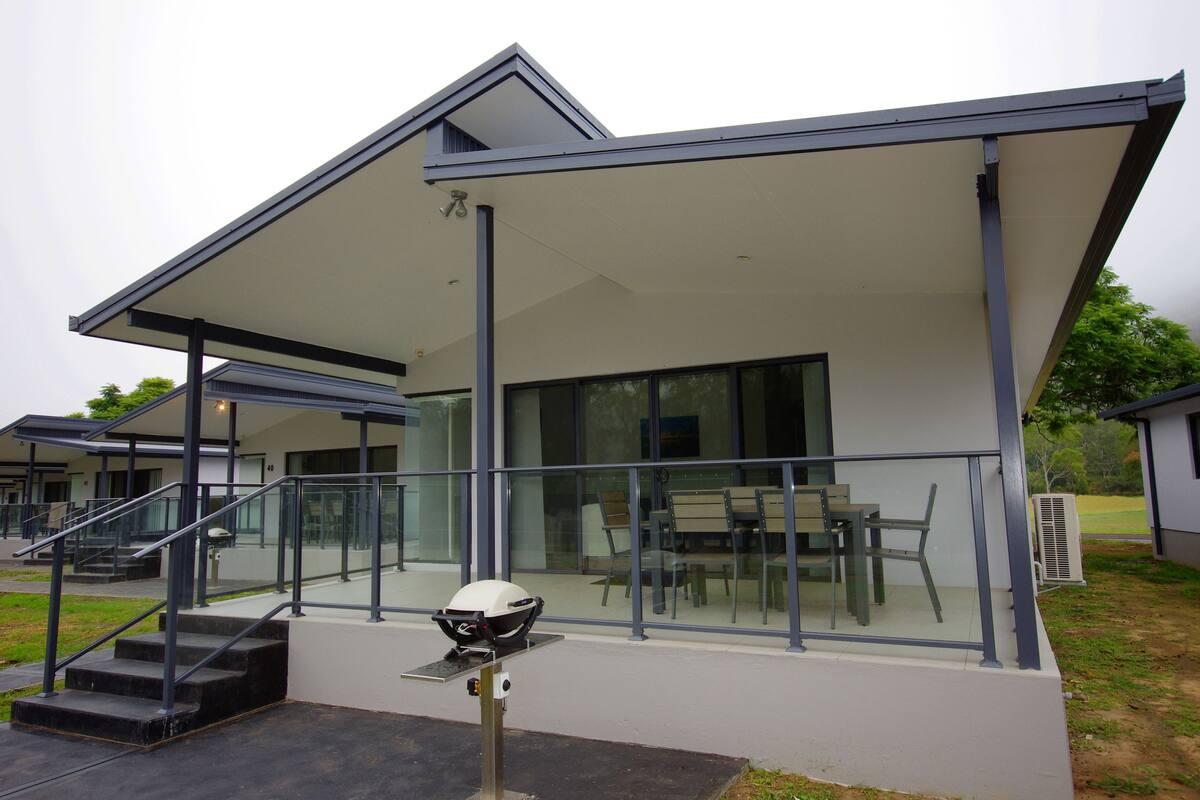 A modern building with a covered patio, glass railings, and a seating area.