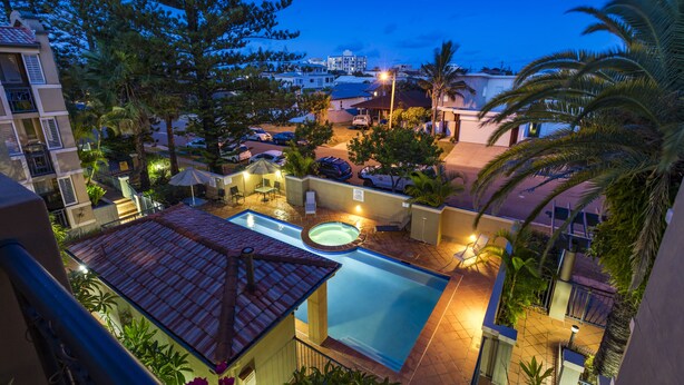 Zona de piscina con hidromasaje, rodeada de palmeras y vistas a una zona residencial al anochecer.