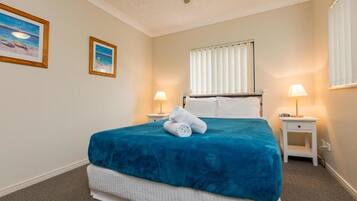 A hotel room with a bed, two bedside tables, a window with blinds, and two framed pictures on the wall.