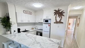 Una cocina moderna con encimera de mármol, armarios blancos y un letrero que dice 'BEACH HOUSE'.