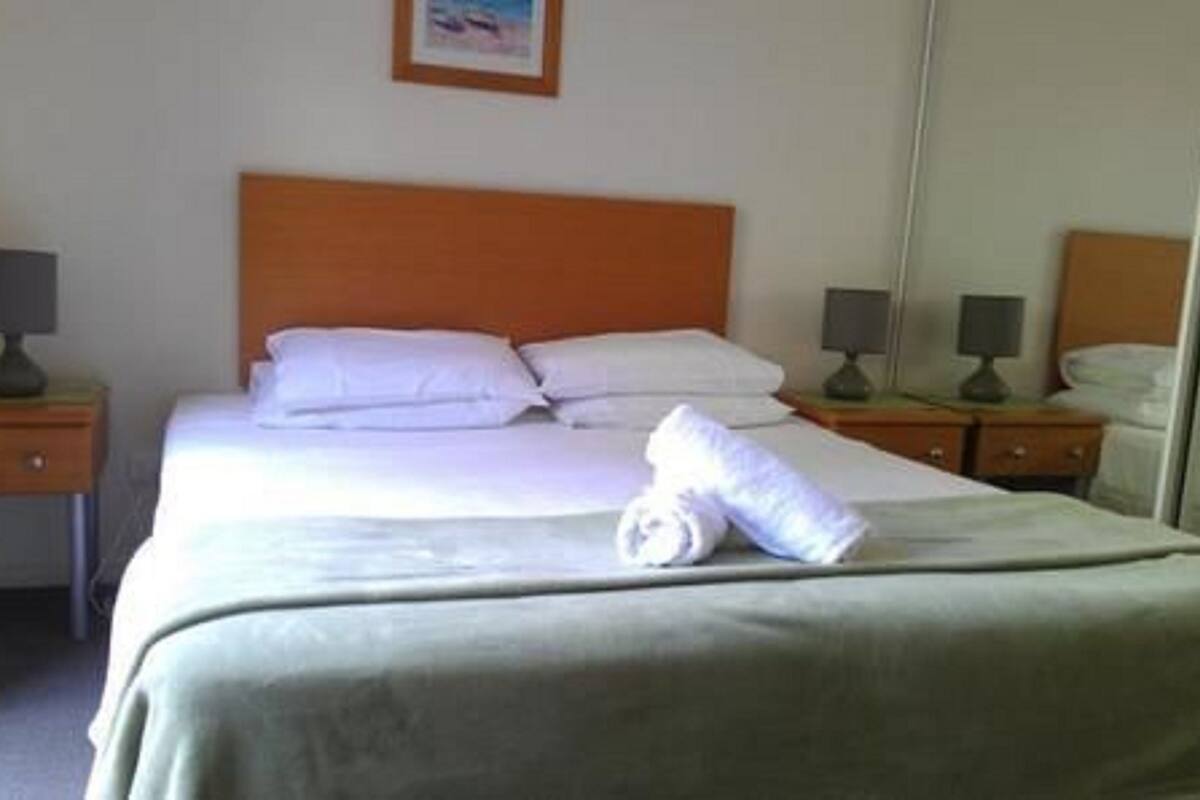 A neatly made bed with white linens and pillows, two bedside tables with lamps, and a mirror on the wall.