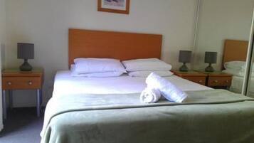 A neatly made bed with white linens and pillows, two bedside tables with lamps, and a mirror on the wall.
