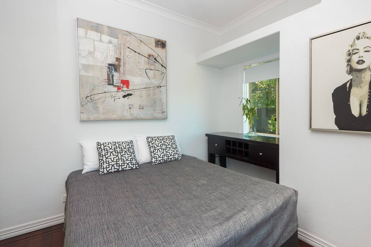 Une chambre à coucher avec un lit, un bureau et deux œuvres d’art accrochées aux murs.