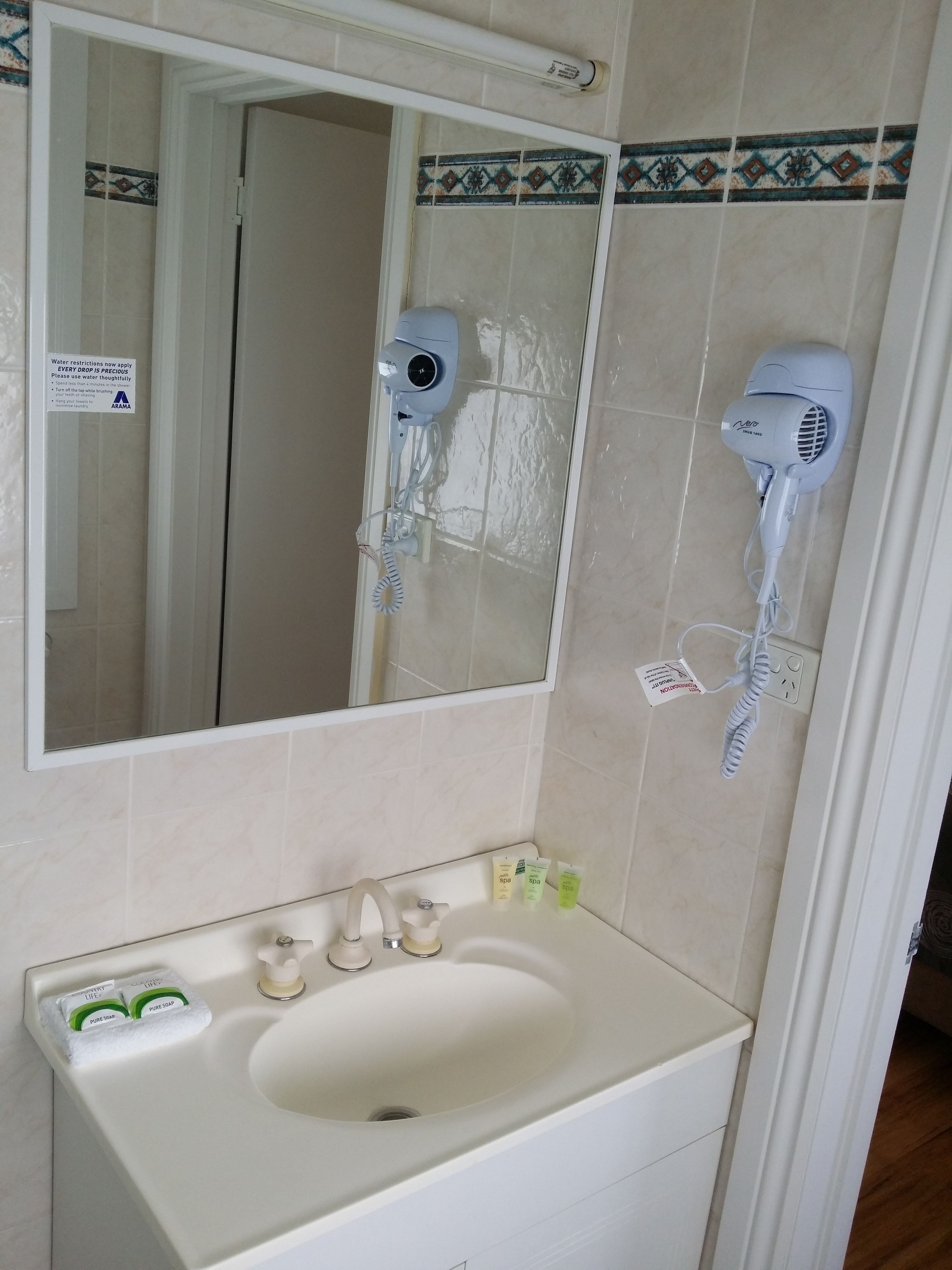 A bathroom with a sink, mirror, two hair dryers, and a towel rack.