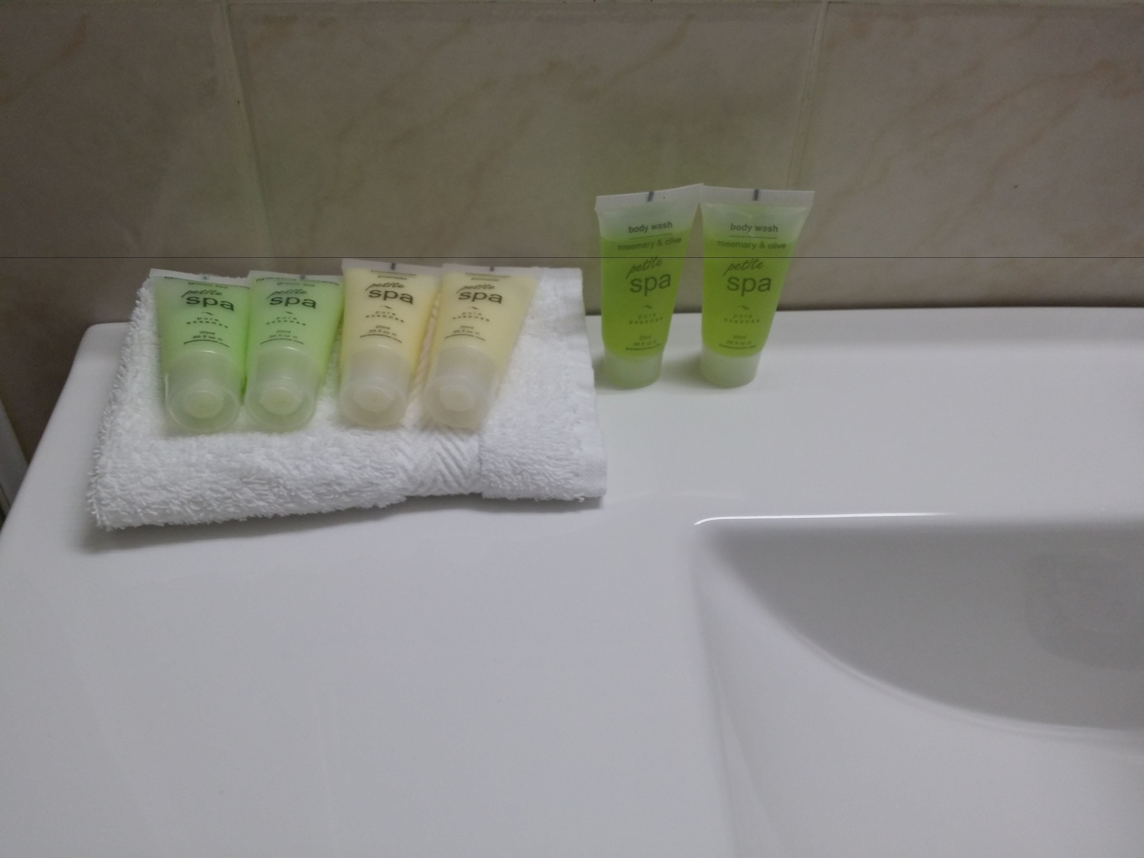 Un baño con un lavamanos blanco y una toalla con cuatro botellas de jabón corporal.