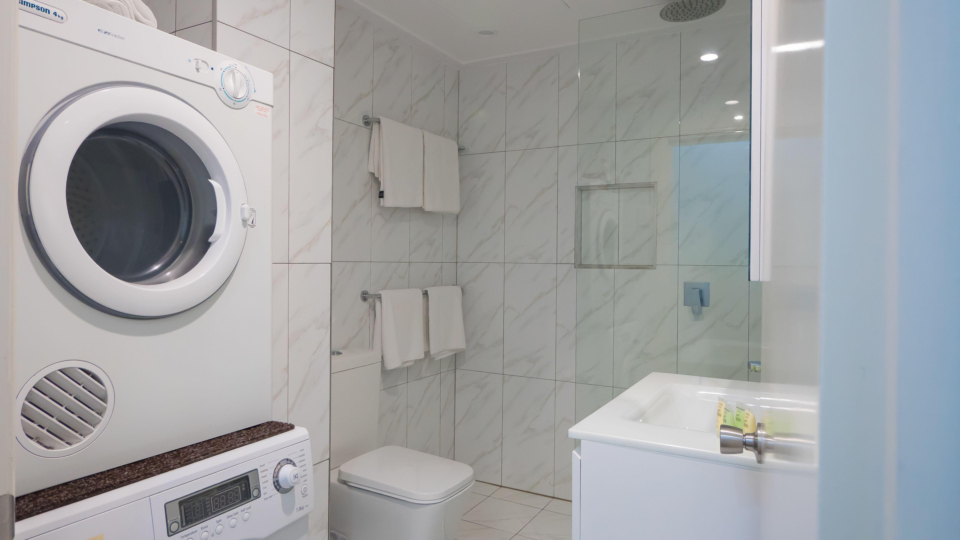 Une salle de bain moderne équipée d’un lave-linge intégré, de toilettes et d’un lavabo avec un miroir.