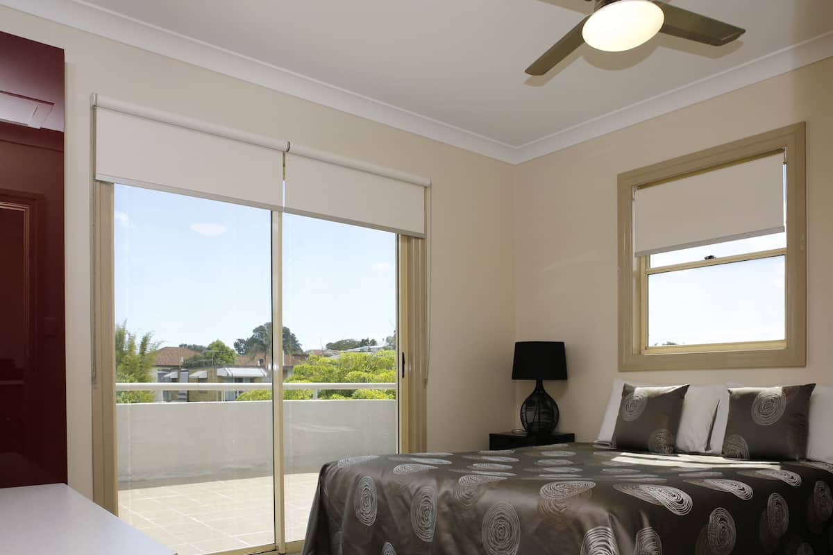 Une chambre à coucher comprenant un lit, une table de chevet, une lampe, un ventilateur de plafond et une vue sur l’extérieur grâce à une porte coulissante.