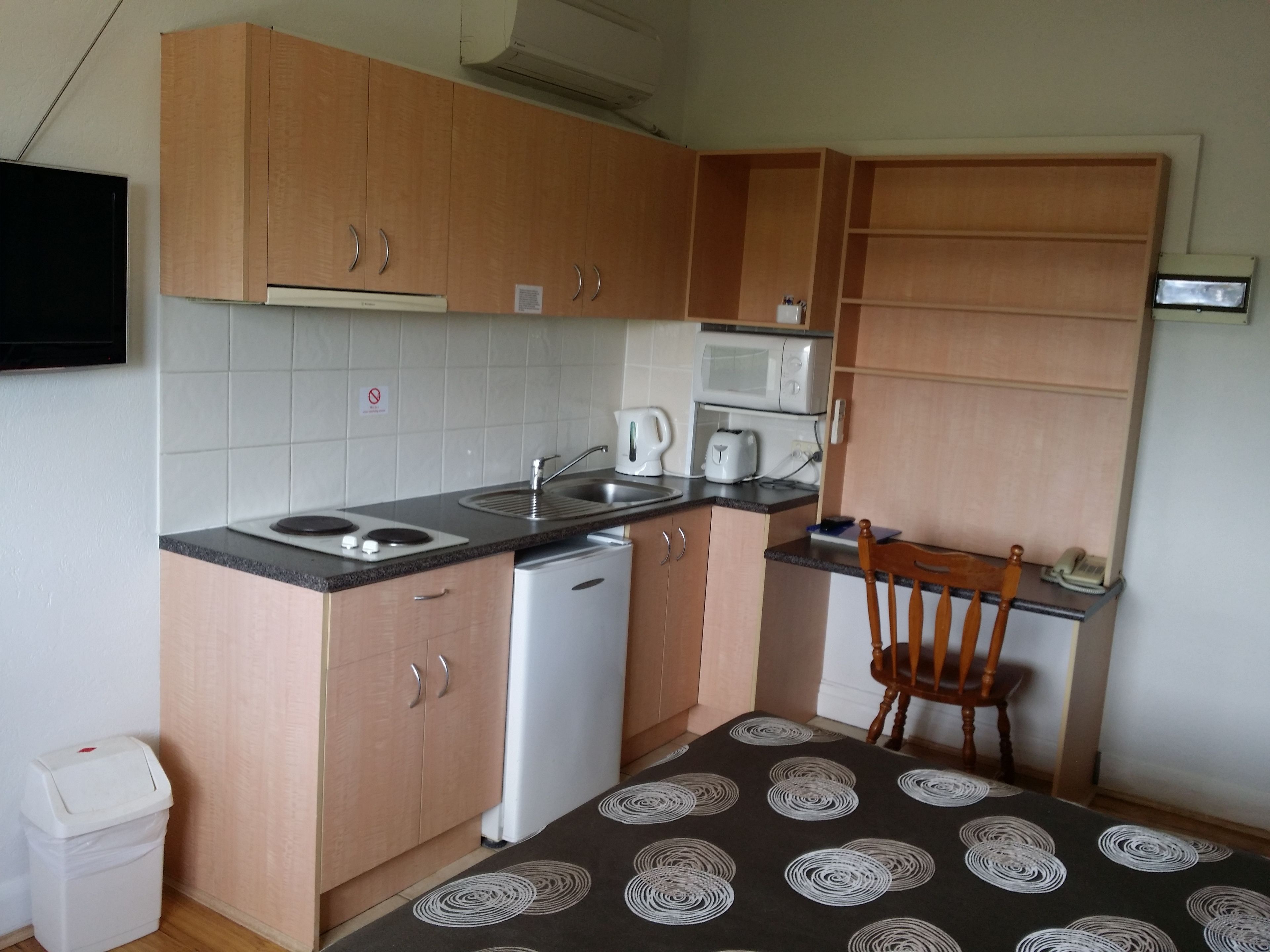 Una cocina compacta con armarios de madera, un microondas, un tostador y un lavabo.