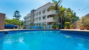 A swimming pool with a clear blue water, surrounded by a fence, and a multi-story building in the background. - Hampton Court Apartments (Clayfield)