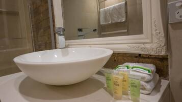 A bathroom with a large white sink, a mirror, and a towel rack. There are three bottles of 'Petite Spa' products on the counter.