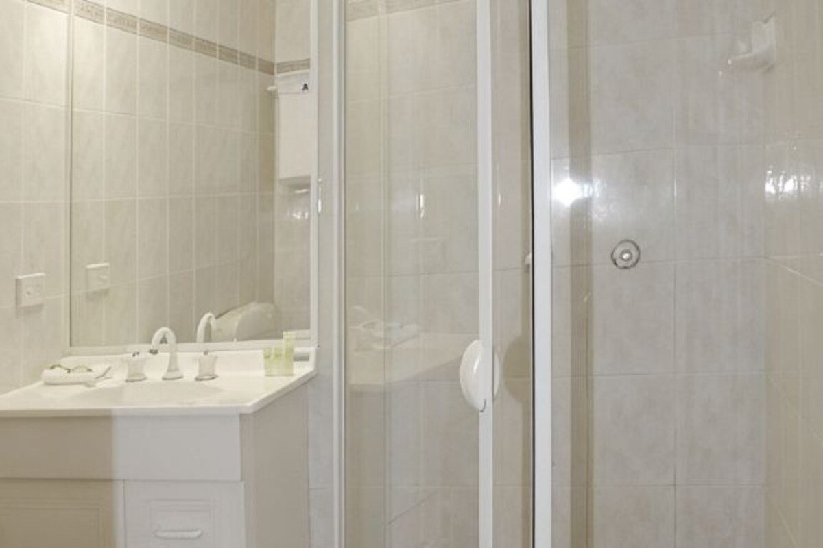 Un baño con cabina de ducha de vidrio, un lavabo blanco y un espejo.